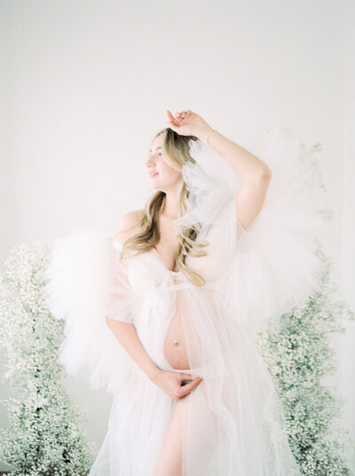 Expectant mother in white tulle dress with baby's breath flowers, captured by edmonton maternity photographer Kahla Kristen