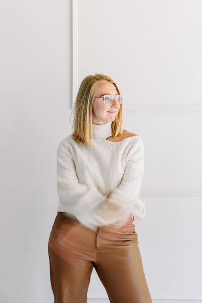 blonde dame, staand, armen gekruist en 1 hand onder haar kin, bril, zwart tope en colbert, grijs geruite broek