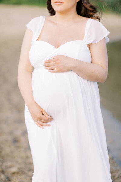 Een prachtige zwangere vrouw in een luchtige witte jurk, vastgelegd in een rustieke outdoor setting.