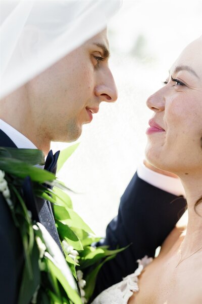 A newlywed couple standing close and looking at each other under a veil 