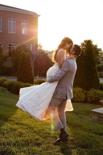 Groom picking bride up and swinging her around while kissing her during sunset