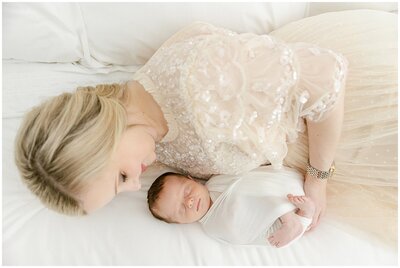 mom and baby laying on bed during in home newborn session with chrissy winchester photography