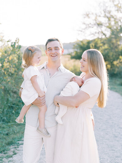 family of four smiling at each other while standing on gravel path at their family photoshoot with louisville family photographer