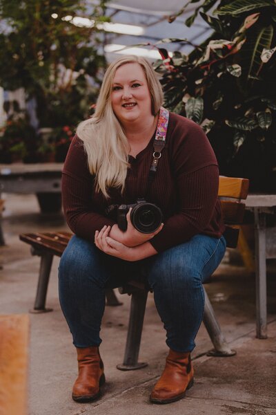 Kyla, owner of Bore Tide Photography, sits in a greenhouse with her camera