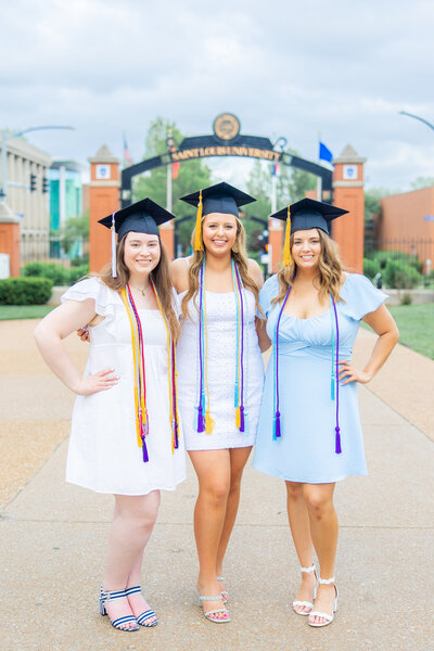 3 SLU senior girls with cute dresses and caps in front of Saint louis university sign