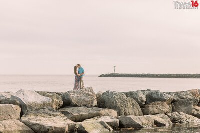 Engaged couple kiss each other while standing on the jetty rocks at Corona del Mar State Beach in Newport Beach