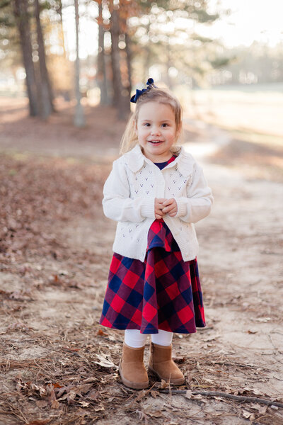 Little girl smiling at camera surrounded by fall scenery.