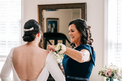 a photo of a mother helping her bride daughter into her dress on her wedding day in connecticut