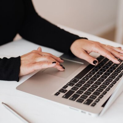 Hands typing on laptop during online hair consultation and referral process for trichology services.
