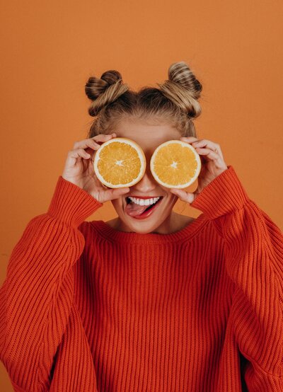 girl with pig tails and orange slices over her eyes wearing an orange sweater with an orange photo background