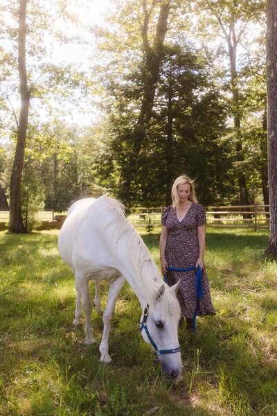 Leiko standing beside her grazing white horse during a private session focused on strengthening horse-human relationships in Massachusetts