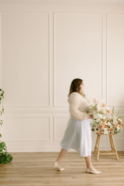 Wedding planner, Zelie & Co., walking across a large room with a large bouquet of flowers in her hand