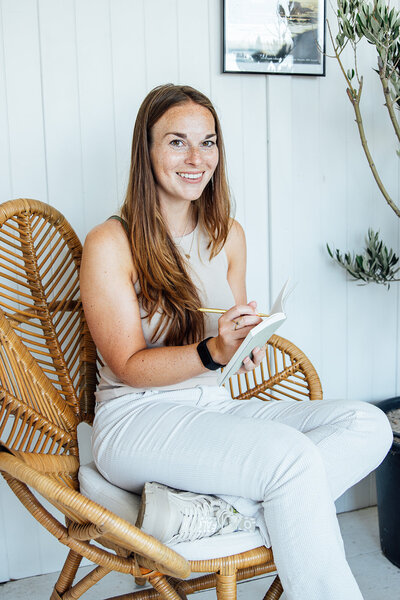 Eva (schrijver en schrijfcoach) op stoel, schrijvend in een schrift.