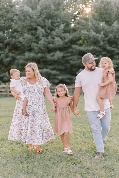 A joyful family walking hand in hand through a sunlit field, smiling together during their outdoor session — Portrait photographer in Raleigh.
