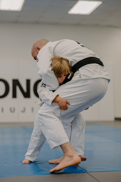 Kid in gi grappling with the black belt instructor in a kids bjj class