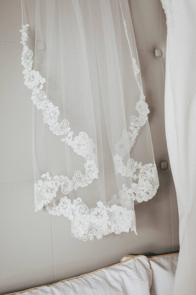Wedding veil with flower hem hanging on white leather bed head board