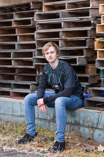 saint thomas of aquainis high school senior guy sitting on blue concrete ledge with pallets in the background, hartville, ohio, photographed by jamie lynette photography