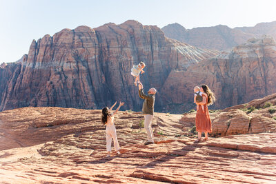 family playing together and dad throwing little girl in the air at the red rocks at snow canyon state park photo by st george photographer sadie peterson