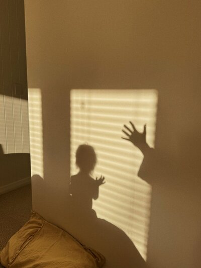 Warm evening light casting playful shadows of a child and an adult’s raised hand on a beige wall