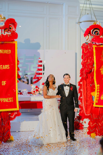 Bride smiles while the groom kisses her cheek in front of a white floral arch.