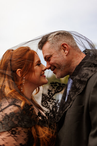 A wedding photograph of a couple in black about to kiss