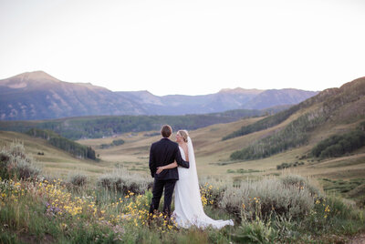 Wedding couple standing in wildflowers with mountain backdrop