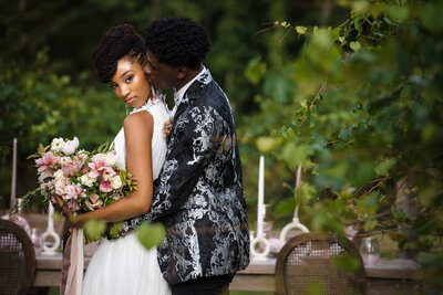 Groom whispering into bride's ear while bride cradles her bouquet and looks fiercely into camera at North Corner Haven