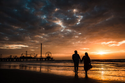 Couple walk on the beach during sunrise on Galveston Beach in Texas.