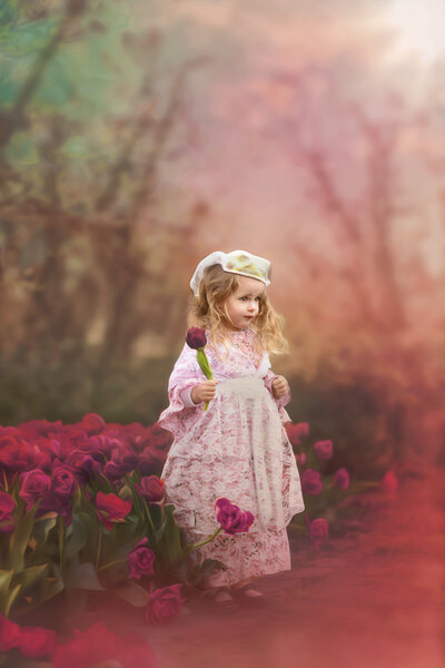 A little girl stands among tulips and stares into the distance. 