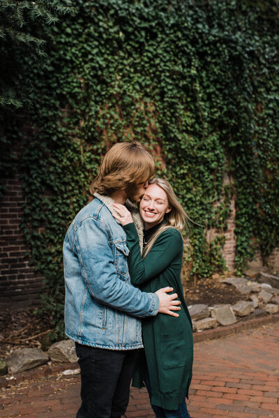 A couple hugging each other in front of a brick vine wall.