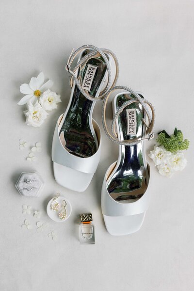 Styled flatlay with wedding details. Designer wedding shoes styled with rings, jewelry, and flowers.