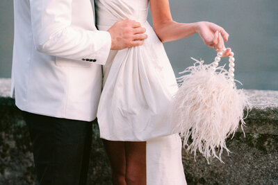 Bride holding fluffy handbag standing at the each of Lake Como by Destination wedding photographer, White Orchid Photography