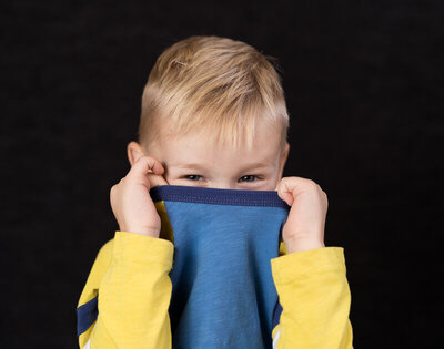 A little boy peeks playfully over his pulled up shirt collar during his school picture day with Kate Simpson Photography.
