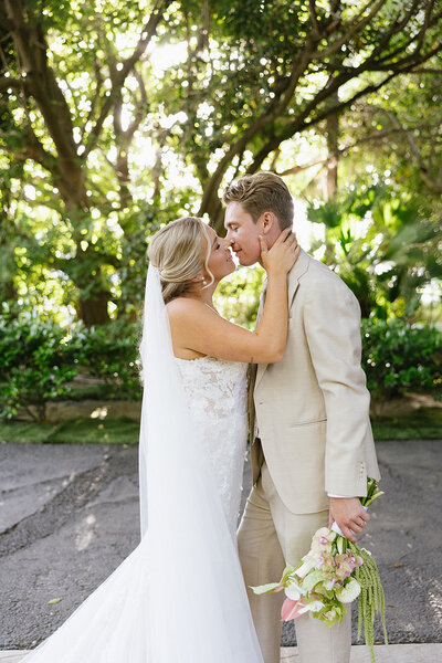 Bride and groom kissing while bride caresses his face 