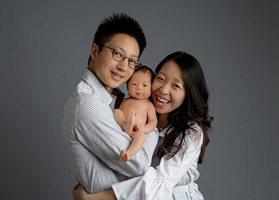 Mom and dad holding their baby between them, smiling at the camera.