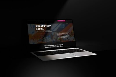 Laptop displaying a website with a dark theme, colorful street art header, and bold white text reading “about b town social,” focused on Birmingham’s independent food and drink scene.