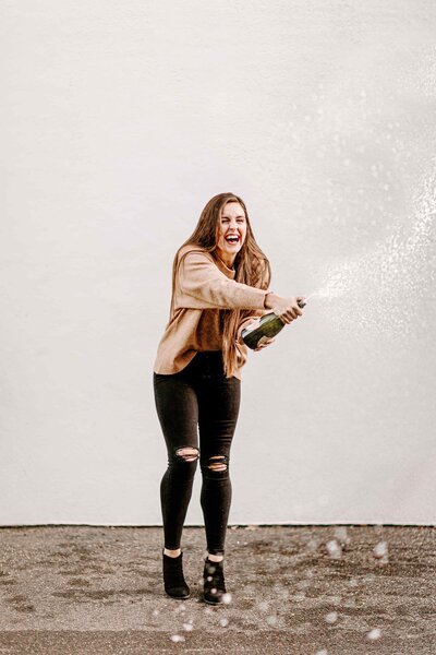 woman laughing spraying a bottle of champagne