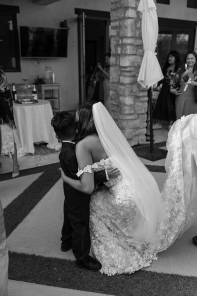 Bride bending down to hug her nephew, in black and white