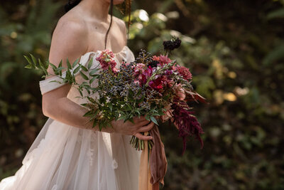 Washington forest elopement. Person in white dress holding a wildflower bouquet