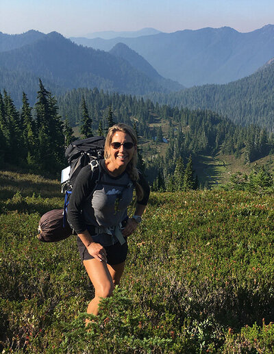 A woman in midlife hiking in the mountains, wearing a backpack and enjoying the scenic outdoor landscape.