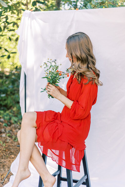 Young lady  looking at flowers while sitting on a barstool with a white backdrop for portraits