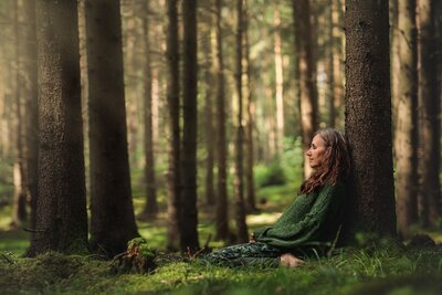 kvinna i gröna kläder, lutad mot ett träd i skogen