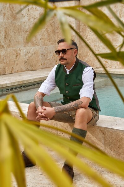 Modisches Männer-Trachtenoutfit mit grüner Weste, traditioneller kurzer Lederhosen und Trachtenschuhe. Perfektes Trachten-Sommeroutfit von Monaco Spatzl – moderne bayerische Trachtenmode 