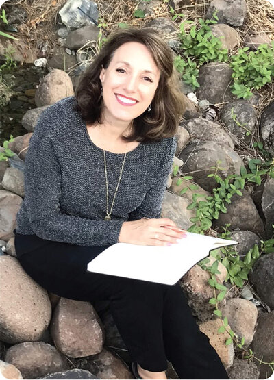 Kelley sitting on some rocks outside and holding a book