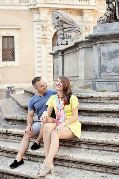 A newly engaged couple sitting on the fountain is Piazza di Santa Maria in Trastevere. Taken by Rome Engagement Photographer, Tricia Anne Photography
