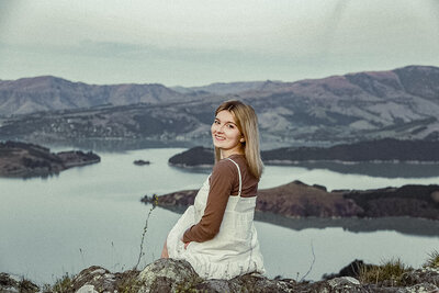 Lavender Turner beams in a candid shot, sitting at the top of a cliff with a stunning natural landscape in the background.