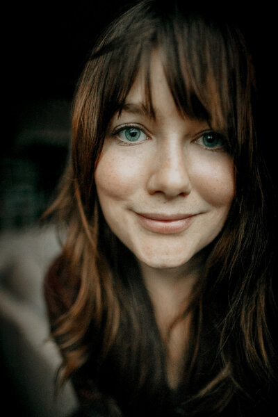 A headshot of Elicia Bryan, a wedding photographer who lives in Atlanta, Georgia. She is looking directly at the camera, has blue eyes and brown hair. Most of the photo is blurry  from the camera's bokeh except for her eyes which makes you feel more connected to them.