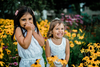 two little girls smile at family portrait photo session with flowers