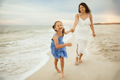 Motherhood session pensacola beach with mom holding daughters hand and running together