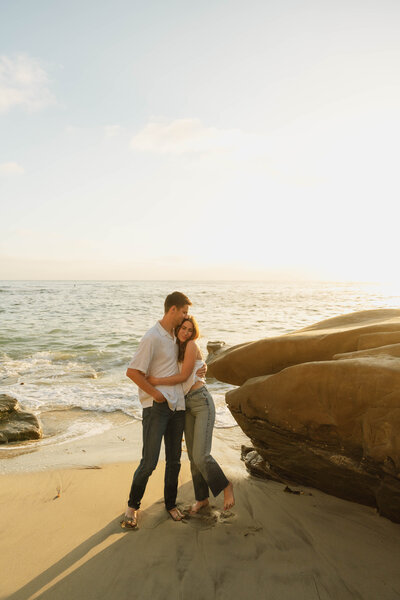 a man and woman hugging each other on a beach during sunset